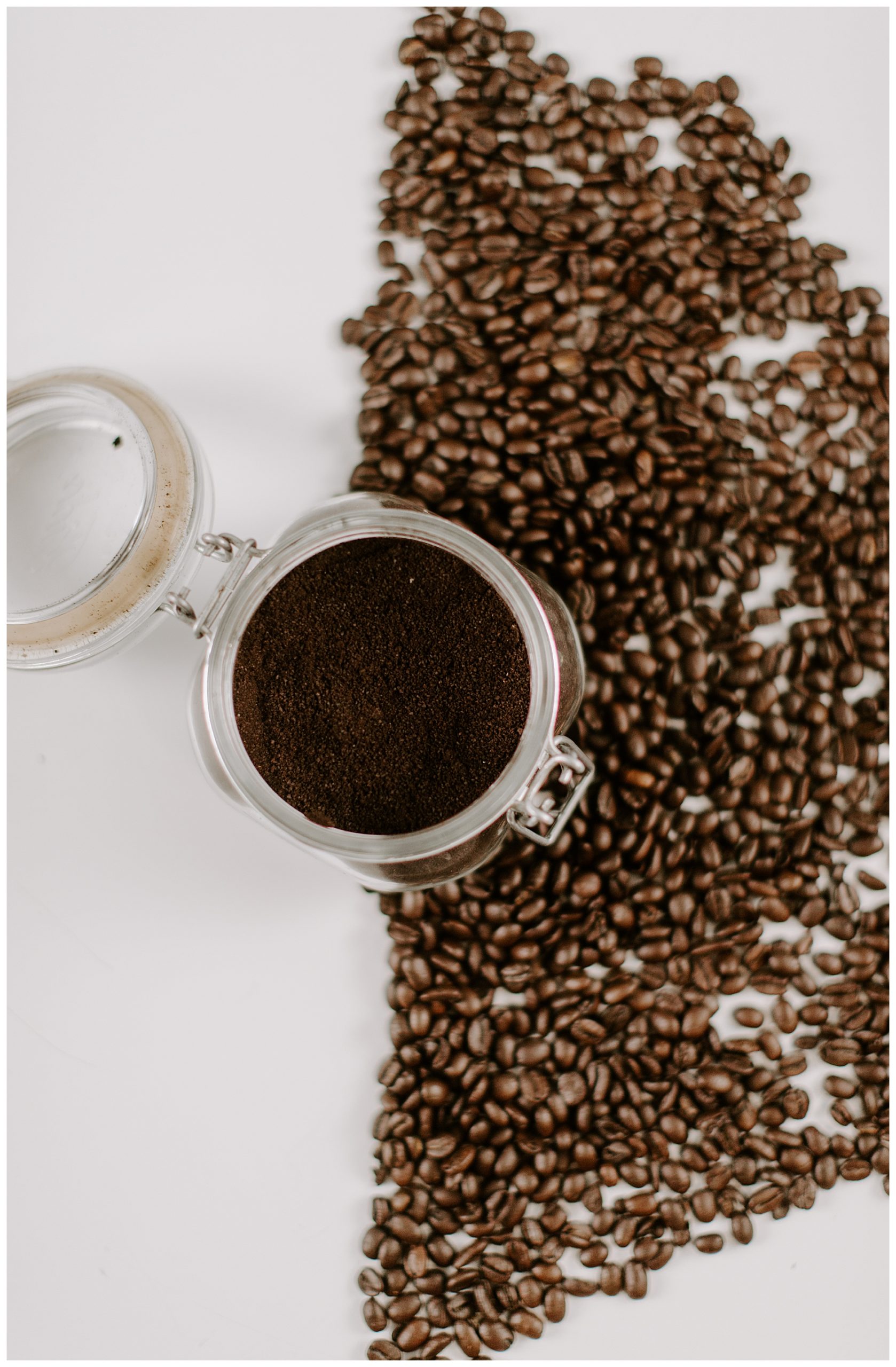 Glass container of coffee grounds, surrounded by coffee beans on a table