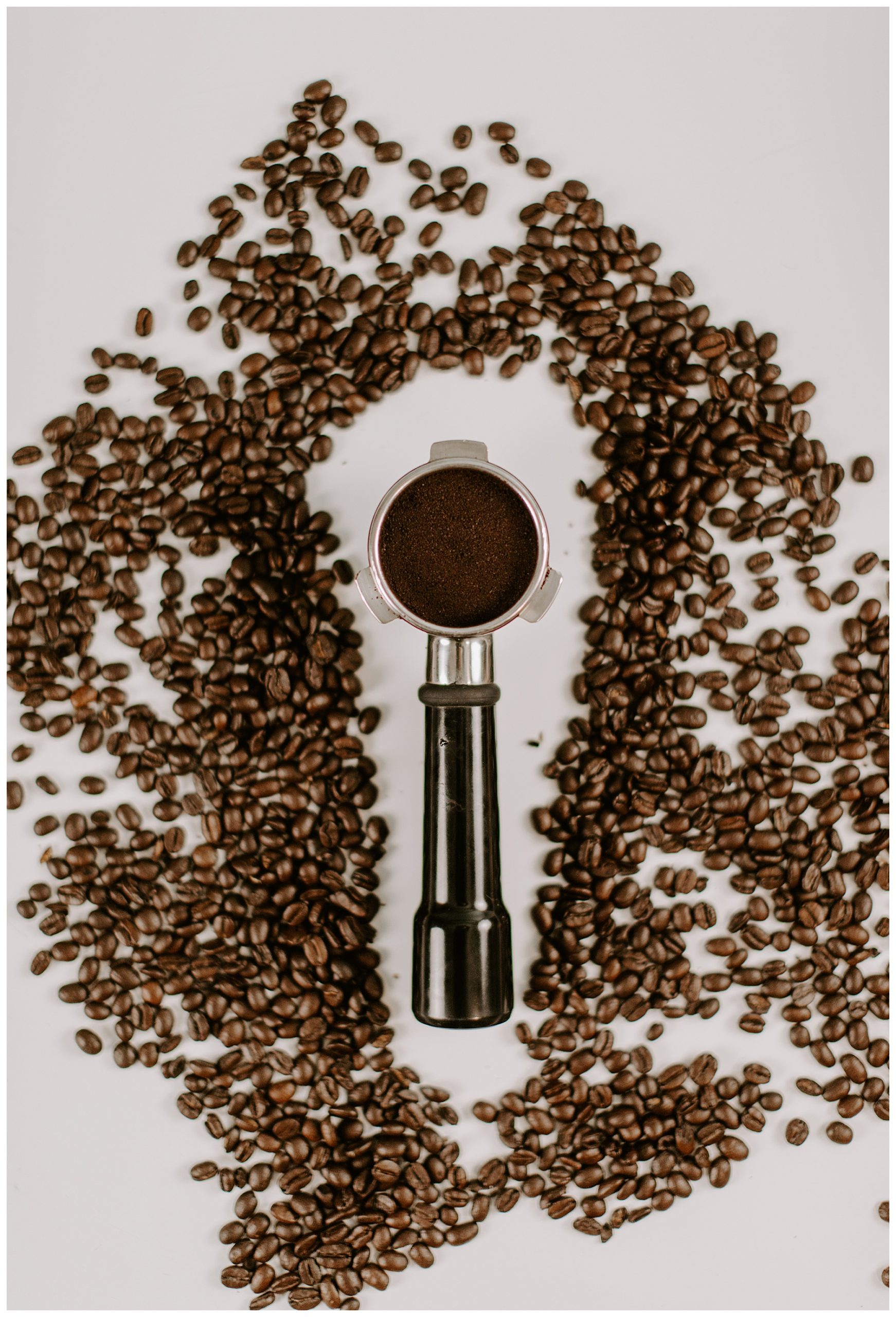portafilter with coffee beans surrounding it on a white table